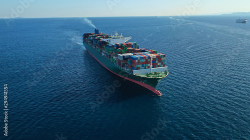 Aerial drone photo of Container cargo Ship carrying load in truck-size colourful containers cruising in deep blue Mediterranean sea 