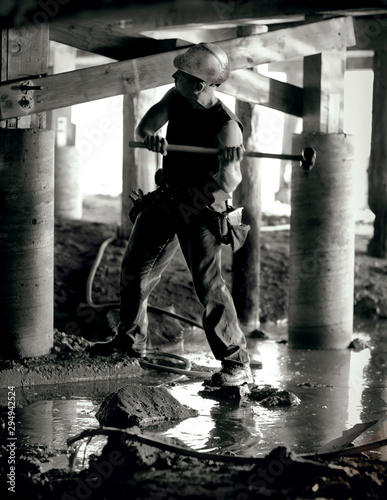 Male construction worker preparing to hit a nail with a large mallet underneath a house. photo