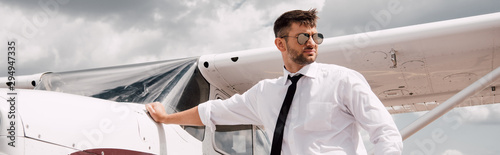 Foto panoramic shot of confident pilot in sunglasses standing near plane