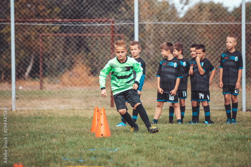 Fototapeta premium Young football player in soccer jersey running between cones and ring ladder marker.