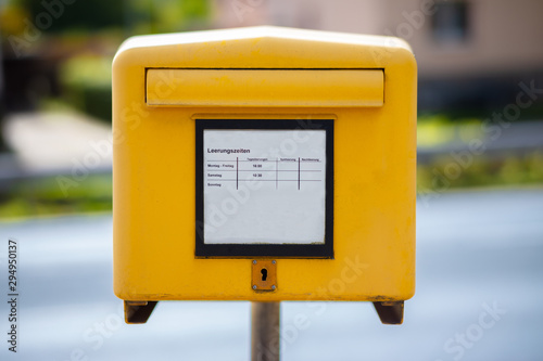 A traditional yellow mailbox at a street in Germany. In the middle, the times are indicated when a discharge takes place. The background is out of focus with nice bokeh.