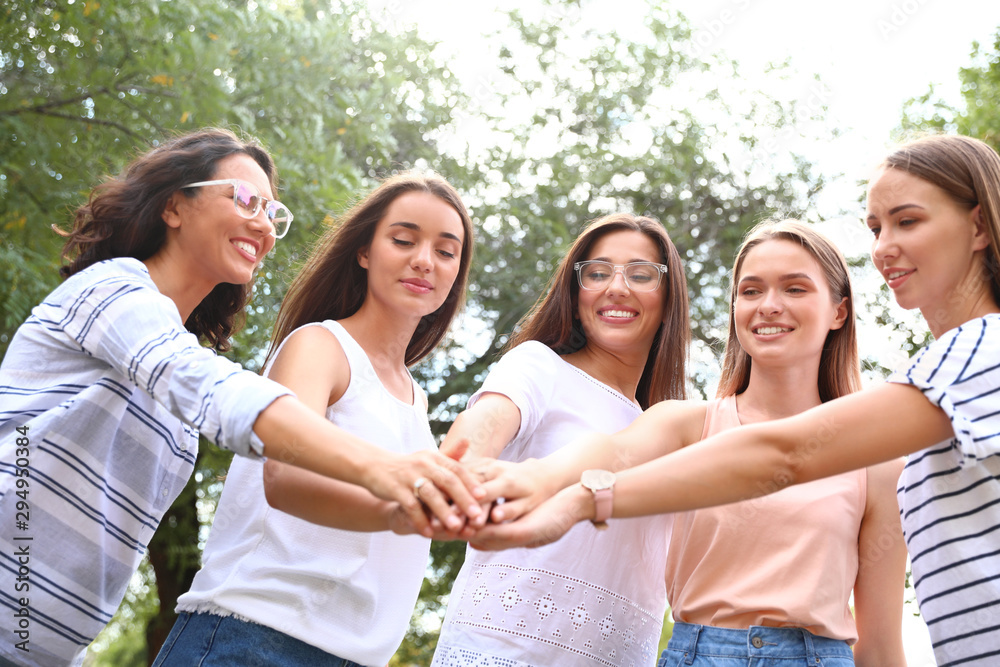 Happy women putting hands together outdoors on sunny day. Girl power concept