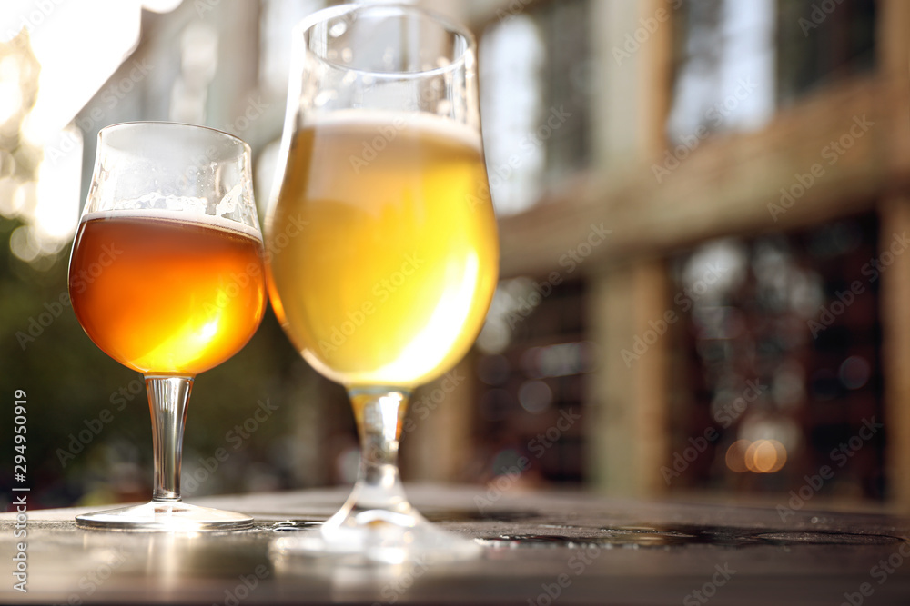 Obraz premium Glasses of cold tasty beer on wooden table outdoors