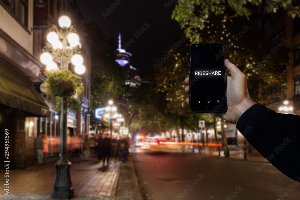 A cell phone with the the words rideshare on the screen superimposed over a view of a city street in Downtown Vancouver.