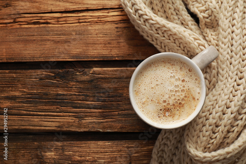 Top view of coffee and knitted scarf on wooden table, space for text. Cozy winter