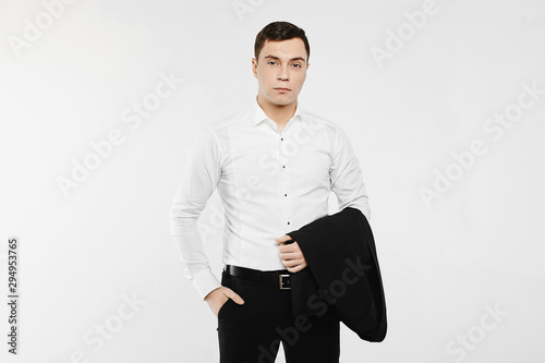 Young businessman wearing in a casual style outfit. The man is posing in a white long sleeve shirt with jeans and holding a jacket on his hand. Concept of men's fashion. photo