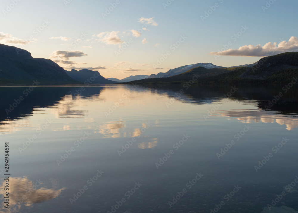Fototapeta premium Beautiful beautiful blue orange sunset over the lake Lulealven in Saltoluokta in Sweden Lapland. Reflection of mountains, clouds and sky in clear the water. Minimalist, copy space