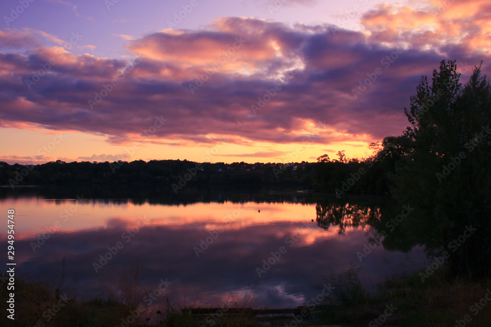 Dramatic sky with cumulonimbus at sunset over the water. Vegetations and foliage in the foreground. Romantic and majestic landscape at countryside. 