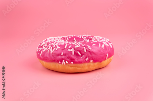 One fresly backed pink glazed donut laying on pink background photo