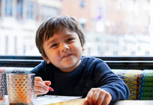 Cropped shot cute lillte boy colouring or drawning on white paper while waiting for food in restuarant, Selective focus of kid enjoy writing with green crayon on paperActivity for children with family photo