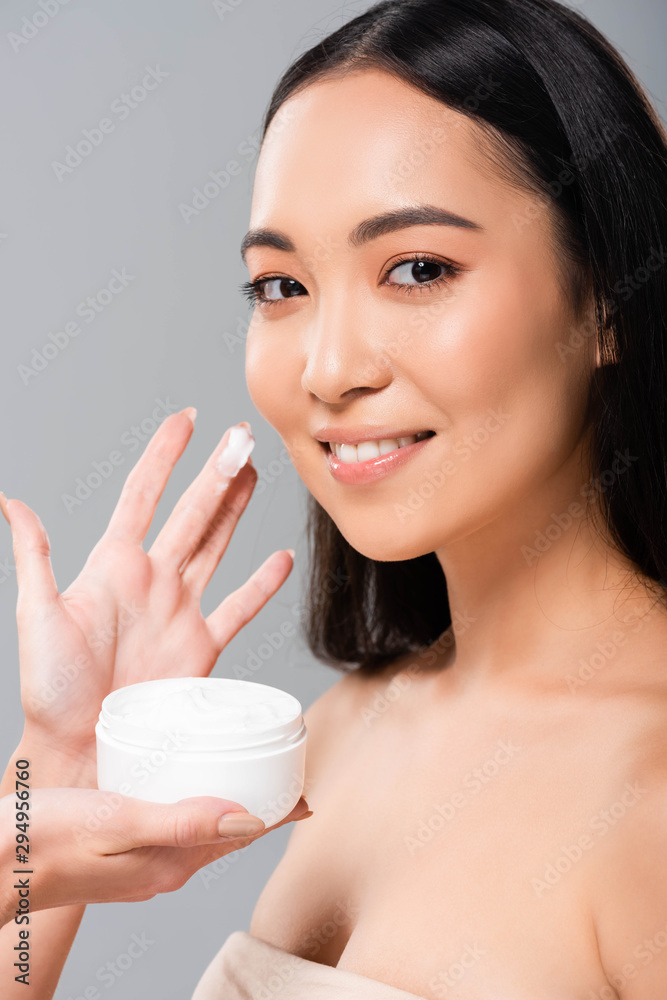 smiling naked asian near woman holding cosmetic cream isolated on grey smiling naked asian near woman holding cosmetic cream isolated on grey