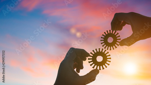 Silhouette two businessmen hands collect old gears into a puzzle, on sunset background. Business concept idea, cooperation, partnership, teamwork.