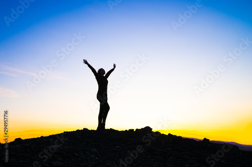 Silhouette of a happy young girl on top of a mountain holding up hands. against the sunset. Success  achievement concept. outdoors
