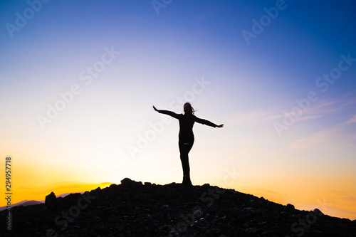 Silhouette of a happy young girl on top of a mountain holding up hands. against the sunset. Success, achievement concept. outdoors