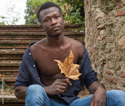 Hombre joven negro de Senegal sentado, con una hoja de otoño en las manos.