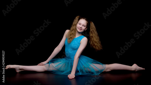 Girl gymnast in the studio on a black background performs gymnas