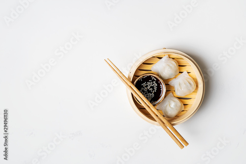 Traditional chinese steamed dumplings Dim Sums in bamboo steamer with sauces and chopsticks on light surface with copy space. Asian food background.