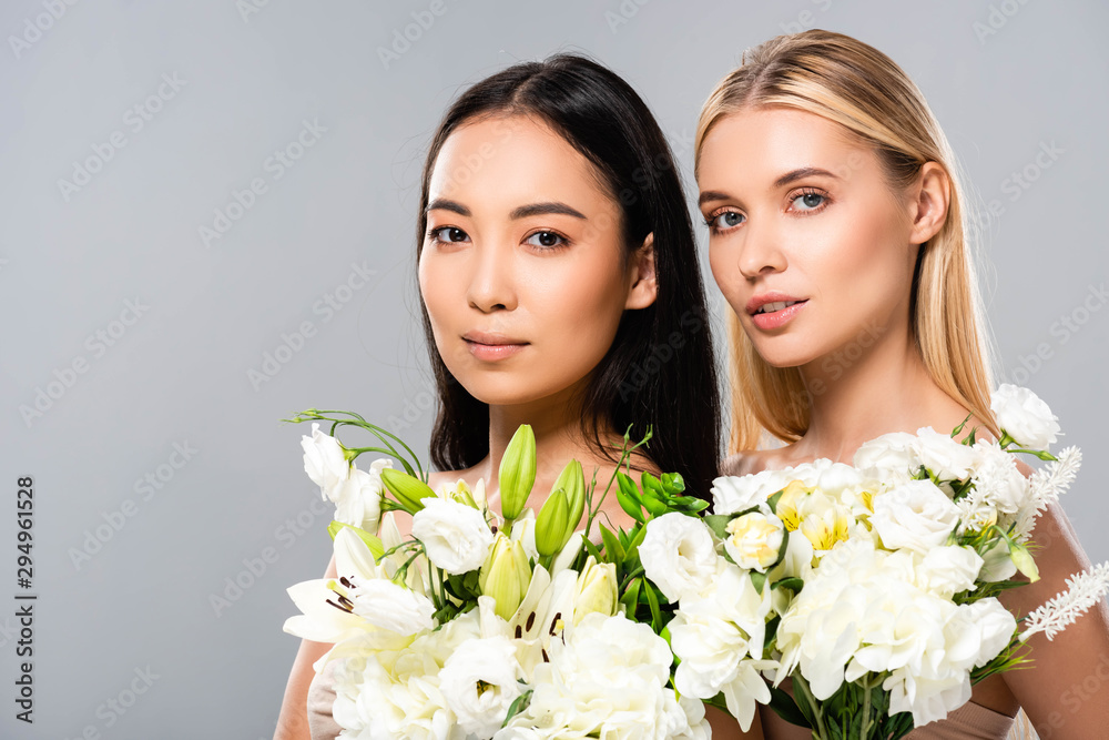 Fototapeta piękna blondynka i azjatycka brunetka nagie kobiety z kwiatami na szarym tle
