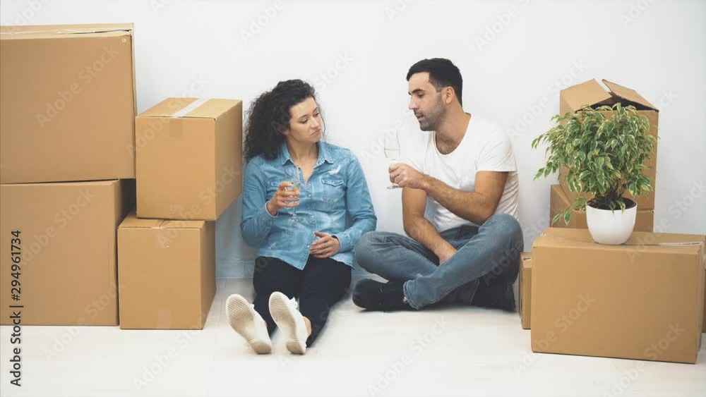 Happy couple is talking while sitting on the floor and holding glasses of white wine. Action. 4K. Happy couple is talking while sitting on the floor and holding glasses of white wine. Action. 4K.