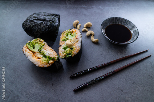 Close up view of onigirazu filled with vegan ingredients and soy sauce on a plate. Japanese meal on concrete background. photo