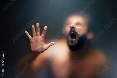 Creepy looking man is screaming behind a frosted glass. photo