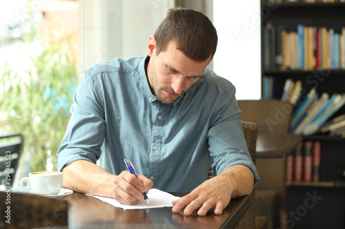 Concentrated man writing notes in a paper in a coffee shop