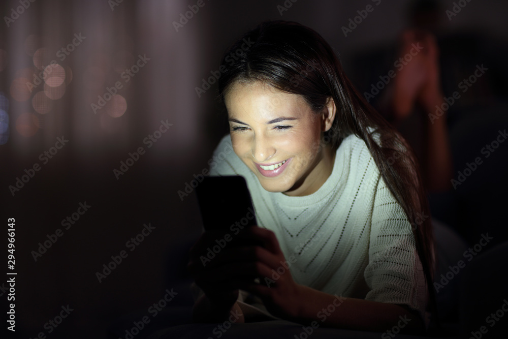 Happy girl checking phone in the night with the face lit Happy girl checking phone in the night with the face lit