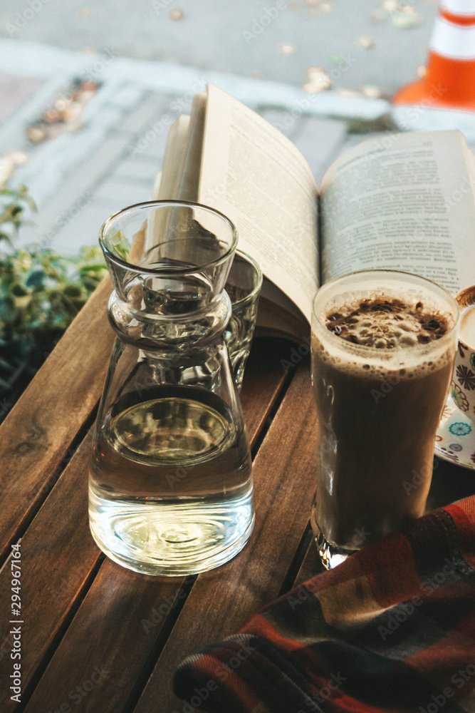 cup of coffee, a book, and a glass on the table and chair