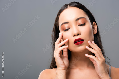 beautiful asian woman with red lips touching face isolated on grey