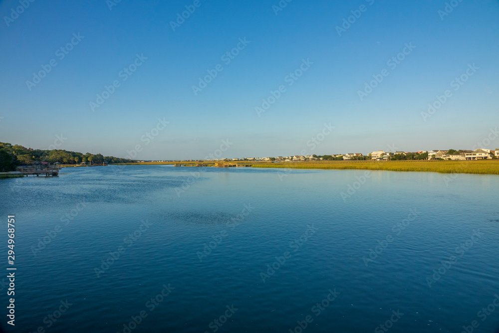 A saltwater creek at high tide in late afternoon sun and the houses that border it.
