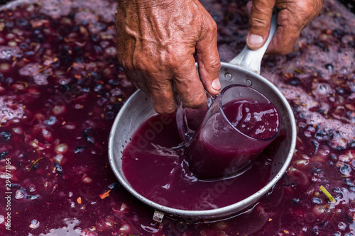 Winemaker's hand with a glass mug, picking up juice from grape must. Wine material, stum, maun. Technology of wine production in Moldova. The folk tradition of making wine.