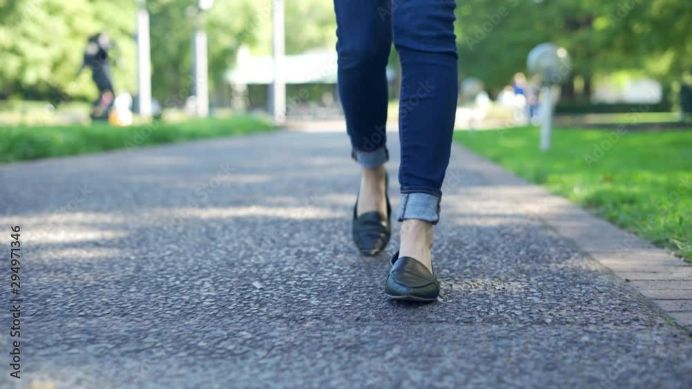 Low angle shot of Young woman walking outside in city park during the day. Focused only on the feet and shoes with shallow depth of field 