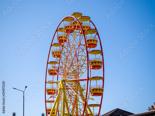 Bright yellow-red ferris wheel against the blue sky. Theme of children's entertainment in the city