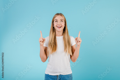 positive smiling blonde girl pointing fingers at copyspace isolated over blue