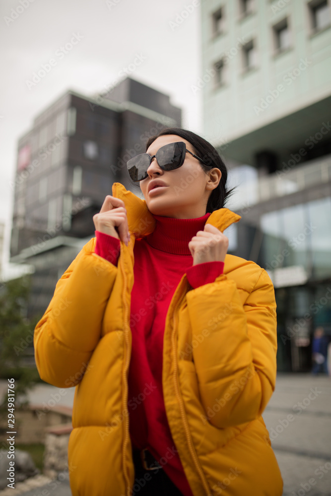 Fototapeta premium Fashion woman in a yellow jacket in the city. On against her building. High-fashion