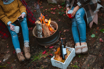 three friends relax comfortably and drink wine on an autumn evening in the open air by the fire in the backyard.