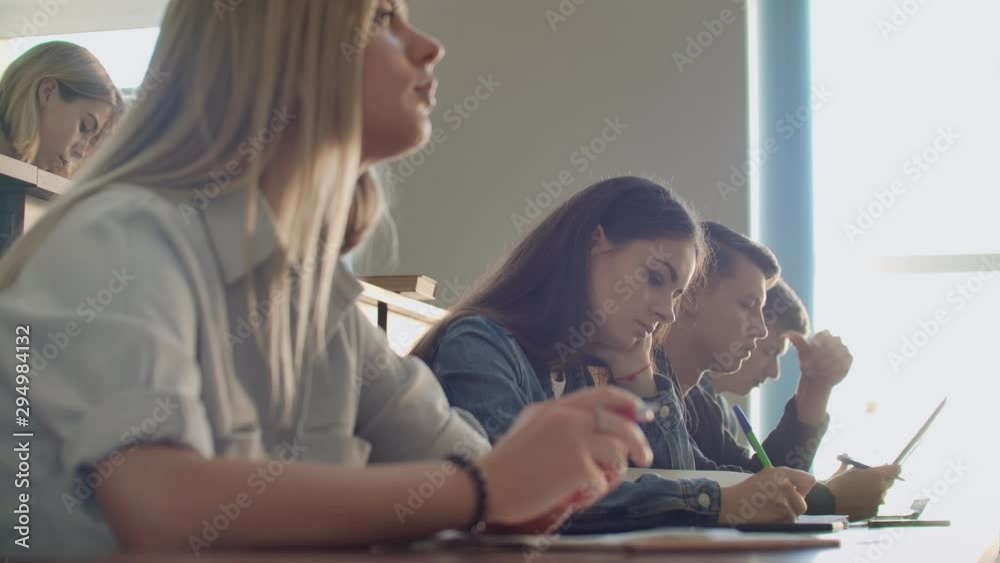A group of male and female students in a large auditorium of the University listen to a lecture by a Professor