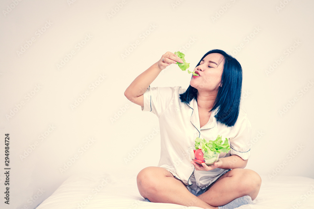 Fat Asian women eat green organic vegetables on the bed. Concept for weight loss for good health Fat Asian women eat green organic vegetables on the bed. Concept for weight loss for good health