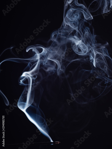 Burning incense isolated on black background, close up view. Structure of smoke, brush effect. Abstract background of smouldering incense stick. Fragrance for meditation and relaxation