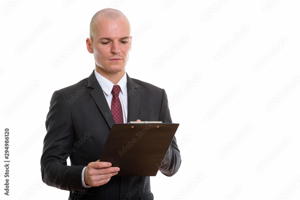 Studio shot of young handsome bald businessman reading on clipbo Studio shot of young handsome bald businessman reading on clipbo