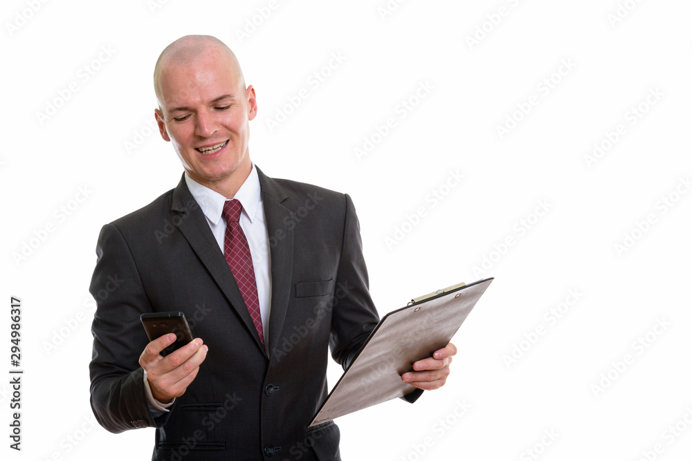 Studio shot of young happy bald businessman smiling and using mo Studio shot of young happy bald businessman smiling and using mo