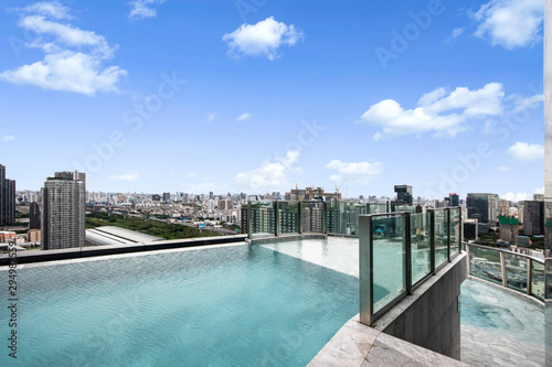 Modern luxury swimming pool with city and sky view on top of condominium building.