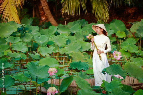 A Vietnamese woman holding a lotus flower in white dress standing on a boat in a pond photo