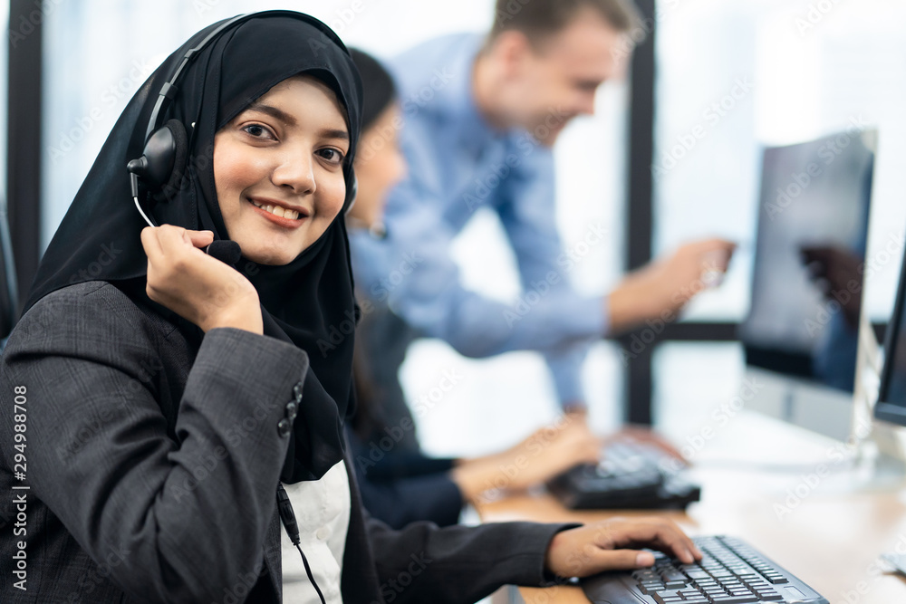 Call center Asian Muslim woman working in office with colleagues. The girl  holding headset microphone and smile to camera. Her co-workers working  behind as background. Customer service concept. Stock-Foto | Adobe Stock