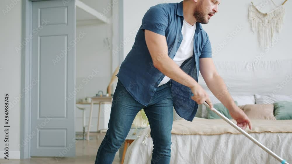 Tilt-down of handsome middle-aged guy washing laminate floor with mop barefoot doing housework in apartment. Household, people and manual work concept.
