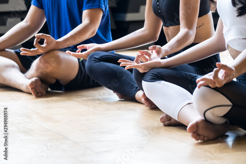 Group of people sitting and making meditation lotus pose in yoga training class. Close up on hands of women and man sitting on the fitness club or gym. Yoga training class concept.