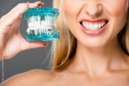 cropped view of naked woman showing teeth and holding jaw model isolated on grey