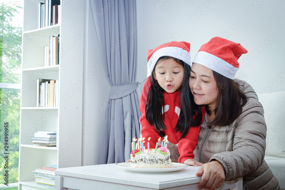 Mother and daughter blowing a birthday cake on Christmas. New year festival concept Mother and daughter blowing a birthday cake on Christmas. New year festival concept