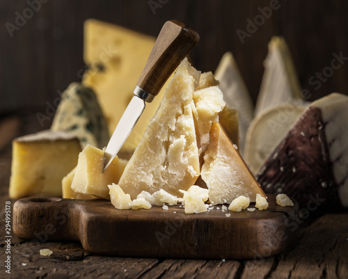 Piece of Parmesan cheese  on the wooden board. Assortment of different cheeses at the background.