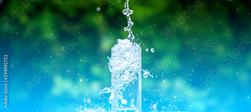 Drink water pouring in to glass over sunlight and natural green background.Select focus blurred background.